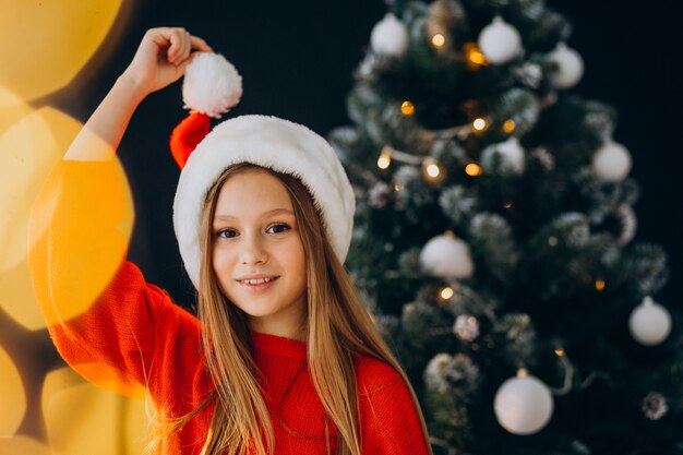 Adolescente linda chica con sombrero rojo de santa por árbol de Navidad