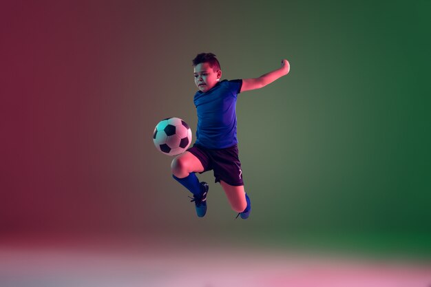 Adolescente masculino de fútbol o jugador de fútbol, niño sobre fondo degradado en luz de neón - movimiento, acción, concepto de actividad
