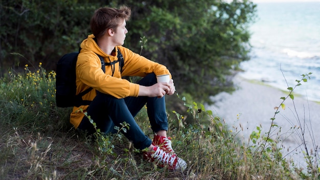 Adolescente con mochila sentados en el suelo en el bosque