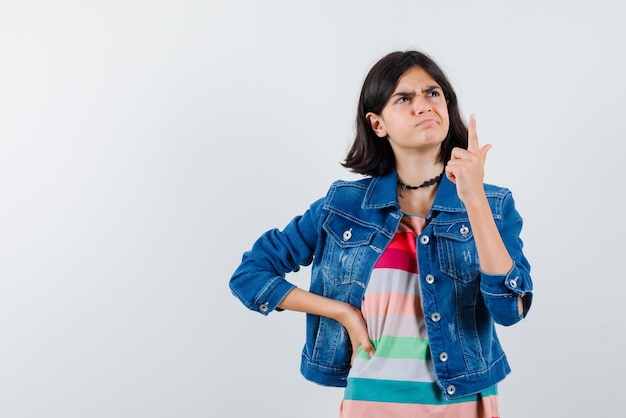 Adolescente mostrando la parte superior con el dedo sobre fondo blanco.