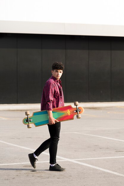 Adolescente negro en camisa a cuadros caminando con longboard