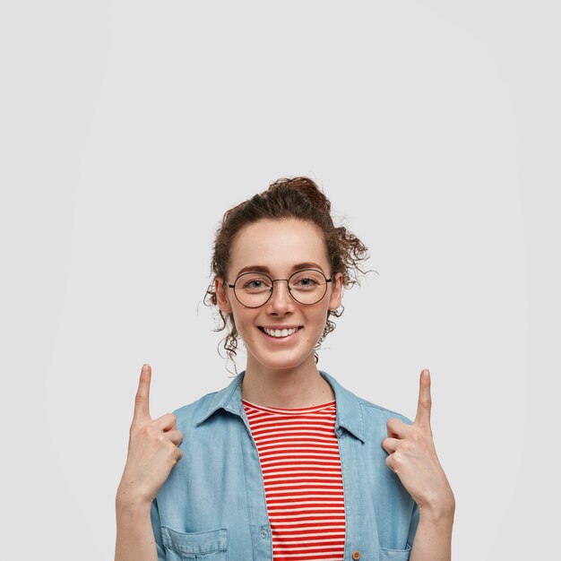 Adolescente pecosa con gafas posando contra la pared blanca