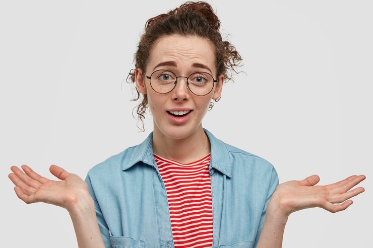 Foto gratuito adolescente pecoso vacilante con gafas posando contra la pared blanca