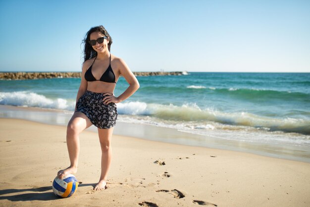 Adolescente con pelota de voleibol. Linda chica en gafas de sol de pie a costa del mar