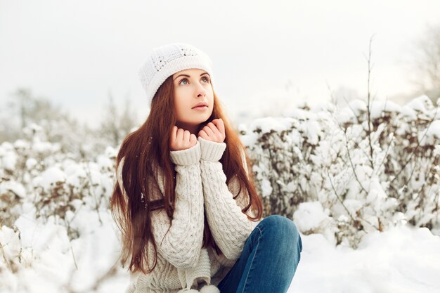 Adolescente pensativa sentada sobre suelo nevado