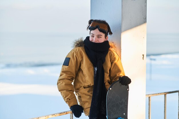 Adolescente pensativo con snowboard en las manos está posando para el fotógrafo en el día de invierno.