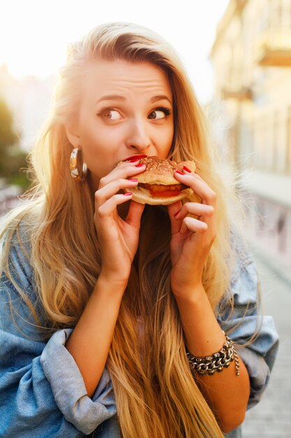 Adolescente que come una hamburguesa en la puesta del sol