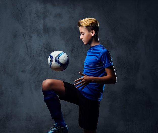 Foto gratuita adolescente rubio, jugador de fútbol vestido con uniforme azul juega con una pelota.