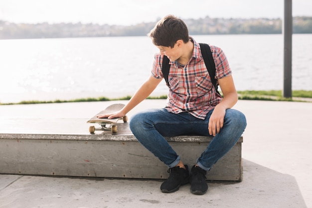 Adolescente sentado en el borde y tocando patín