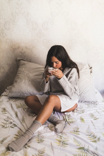 Foto gratuita adolescente sentado en la cama tomando café de la taza