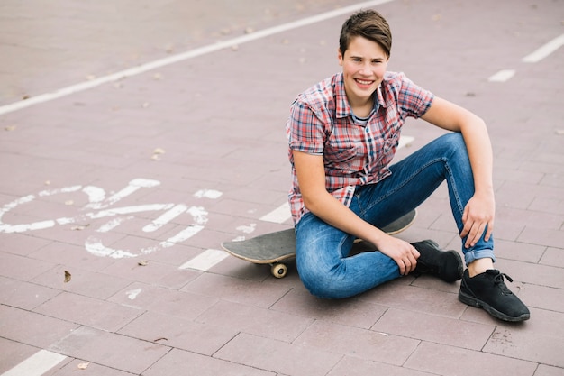 Adolescente sentado en patineta junto al carril bici