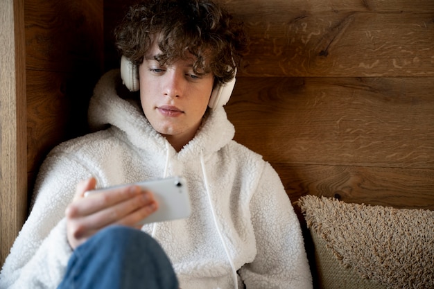 Adolescente sentado en su cama y escuchando música con su teléfono inteligente