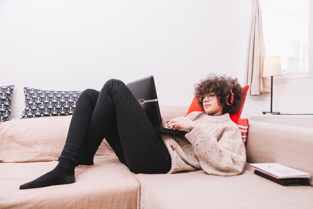 Adolescente en el sofá escuchando música y usando la computadora portátil