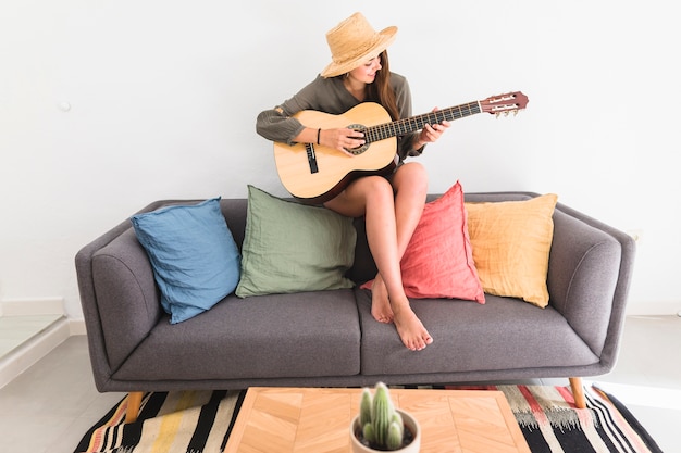 Adolescente con sombrero tocando la guitarra en casa