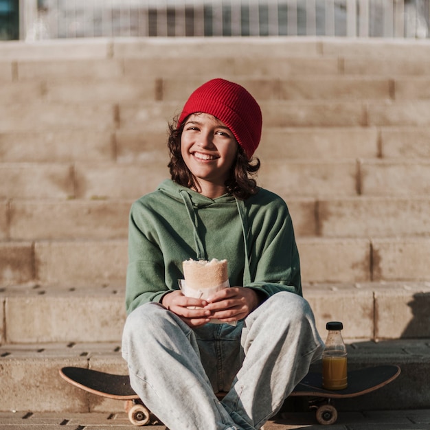 Foto gratuita adolescente sonriente almorzando en el parque en patineta