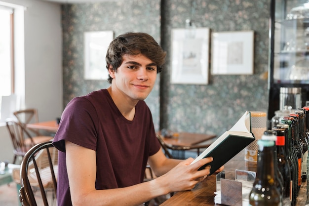 Adolescente sonriente con el libro en el mostrador de la cafetería