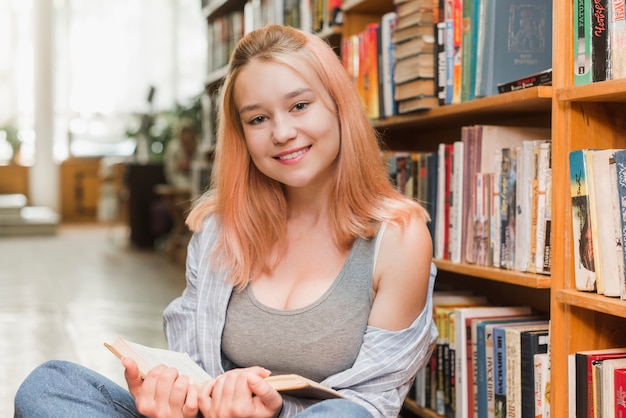 Adolescente sonriente con el libro que mira la cámara