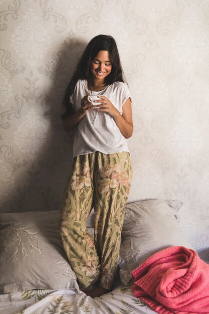 Adolescente sonriente que se coloca en la cama que sostiene la taza de café