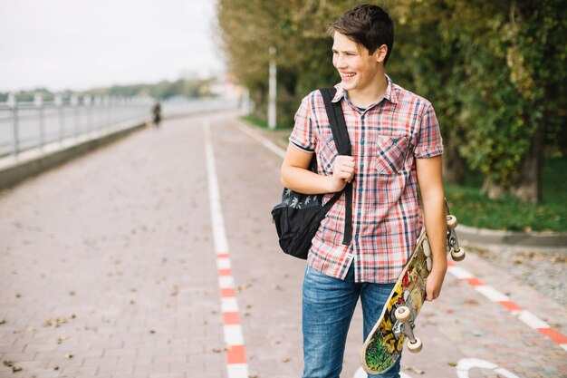 Adolescente sonriente que lleva el monopatín colorido