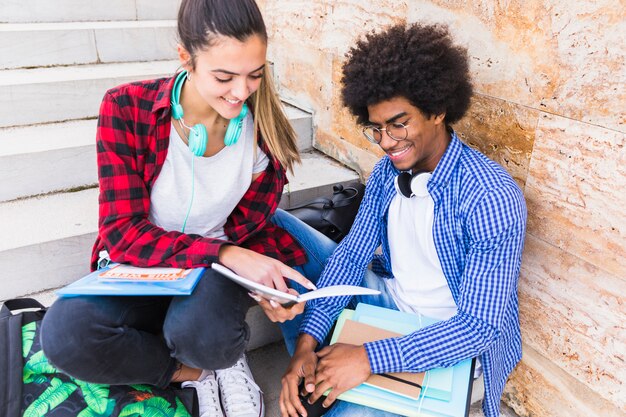 Adolescente sonriente que muestra algo en el libro a su amigo