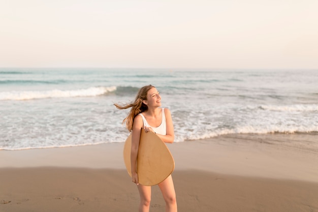 Adolescente sonriente que sostiene el tablero del cuerpo que se coloca en la costa