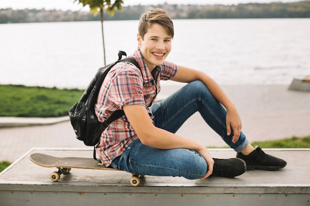 Adolescente sonriente sentado en patineta en la barrera