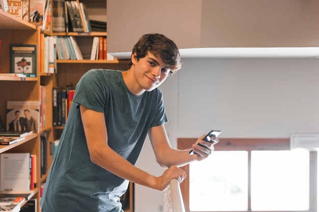 Foto gratuita adolescente sonriente con teléfono inteligente en la biblioteca