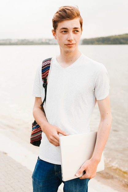 Adolescente sosteniendo portátil junto al lago