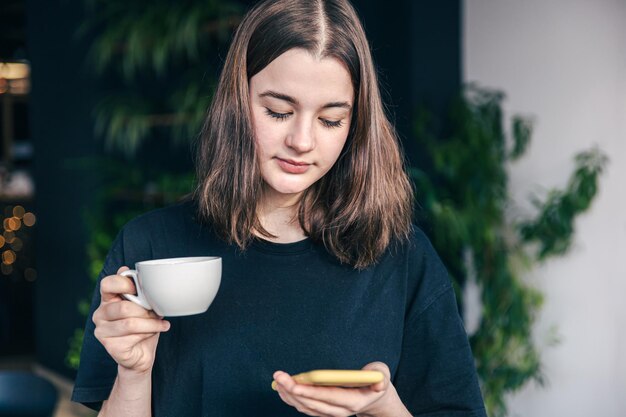 Adolescente con una taza de té y un teléfono inteligente en las manos