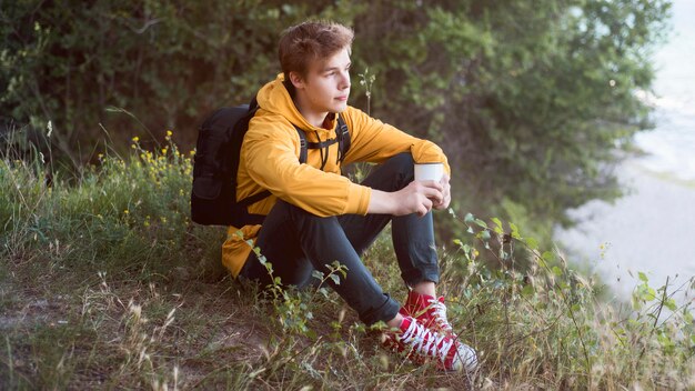 Adolescente de tiro completo sentado en el suelo en el bosque