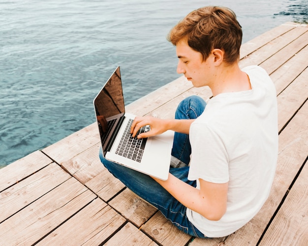 Adolescente usando laptop en el muelle