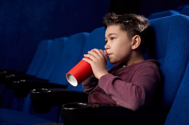 Adolescente viendo películas, bebiendo bebidas gaseosas en el cine.