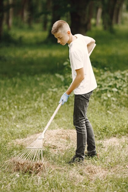 Adolescente voluntario. Niño europeo con guantes recogiendo botellas de plástico en una bolsa de basura negra al aire libre. Concepto de voluntariado y caridad