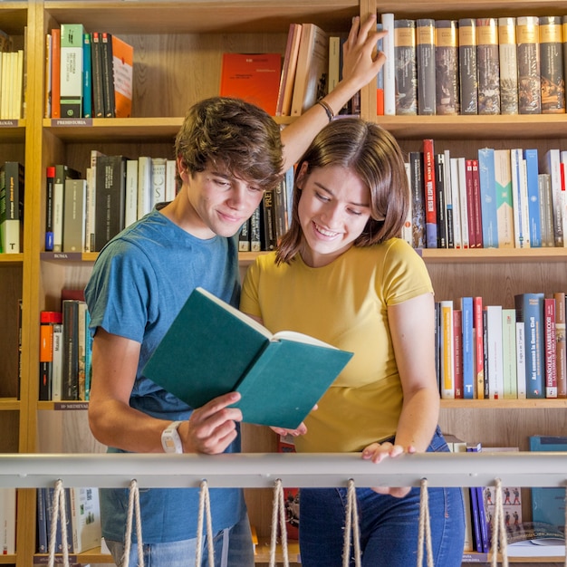 Adolescentes alegres leyendo el libro en la biblioteca