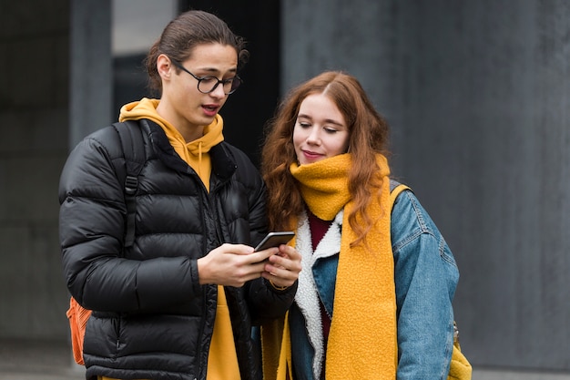 Adolescentes atractivos revisando un teléfono móvil