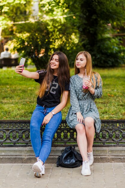 Adolescentes con bebida tomando selfie en el parque