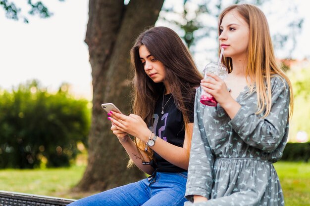 Adolescentes bebiendo cerca de un amigo con teléfono inteligente