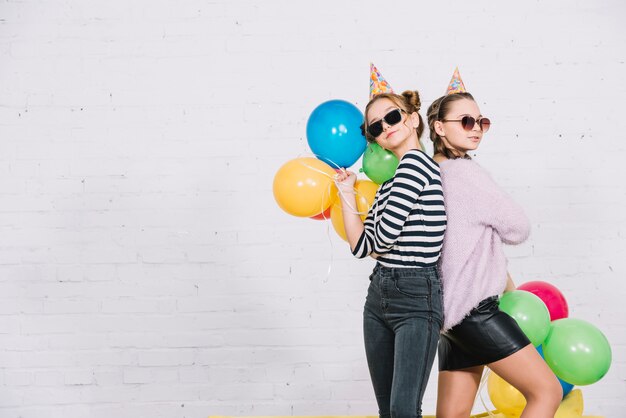 Adolescentes bonitas de pie de espaldas sosteniendo globos de colores en la mano