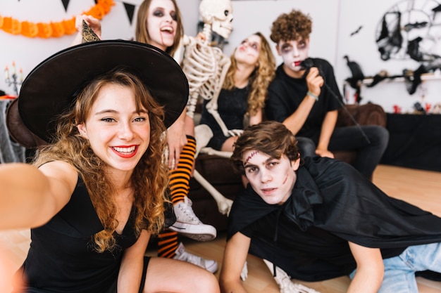 Adolescentes en disfraces de Halloween haciendo selfie en piso