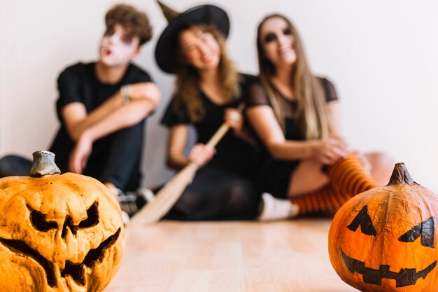 Adolescentes en disfraces de Halloween sentado con calabazas