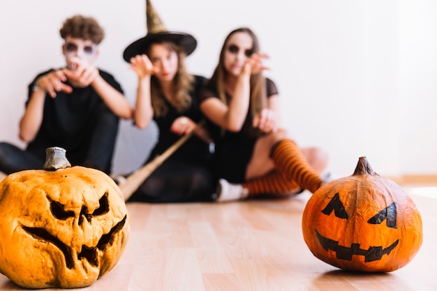 Adolescentes en disfraces de Halloween sentado detrás de calabazas