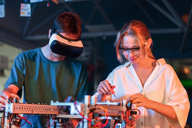 Adolescentes haciendo experimentos de robótica en un laboratorio Chico con auriculares VR y chica con gafas protectoras