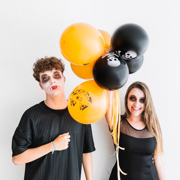 Adolescentes con Halloween sombrío de pie con globos de color naranja y negro