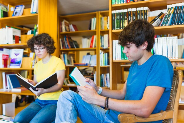 Adolescentes leyendo cerca de estanterías en la biblioteca