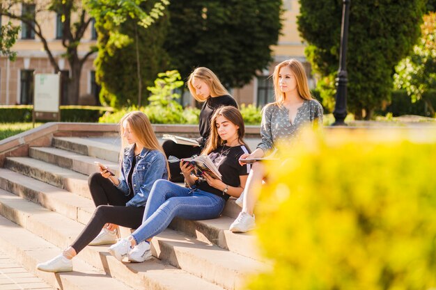 Las adolescentes con libros y teléfonos inteligentes relajantes en pasos