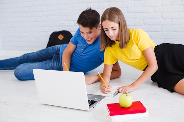 Adolescentes que estudian acostado en el piso cerca de la computadora portátil