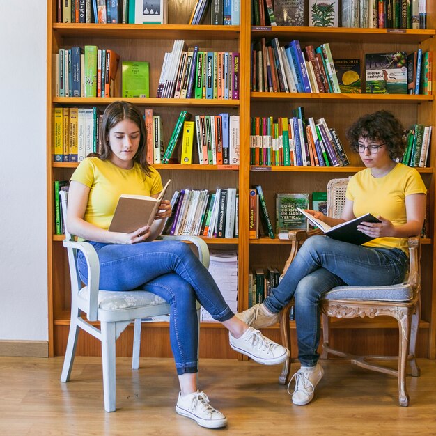 Las adolescentes que leen en las sillas junto a la estantería