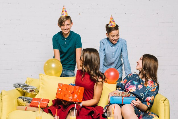 Adolescentes con regalos en la mano mirando a sus novios con sombrero de fiesta