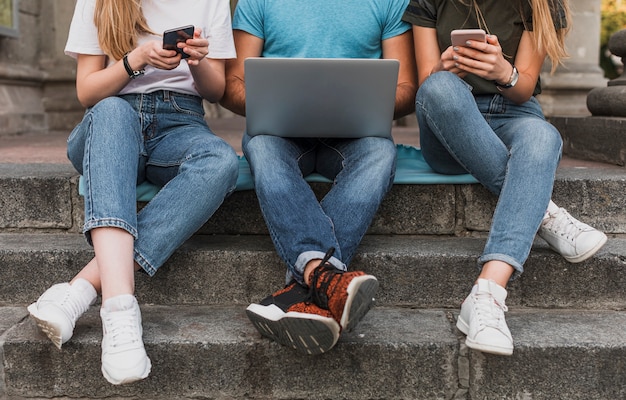 Adolescentes sentados en las escaleras y trabajando en teléfonos y computadoras portátiles