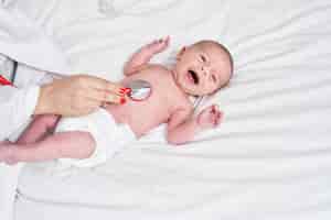 Foto gratuita adorable bebé caucásico sometido a un examen cardíaco con estetoscopio llorando en el dormitorio
